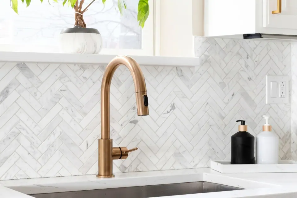 Herringbone marble backsplash with a brass tap